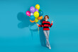 © deagreez - Young woman with balloons in casual striped sweater on blue backdrop, celebrating and enjoying happy moments