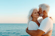 © Anna - Senior couple embracing lovingly near the ocean, with the man kissing the woman’s forehead at sunset