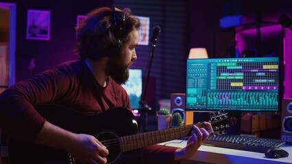 Fototapete - Sound engineer playing acoustic guitar and using mixing console to record music, adjusting volume and adding sound effects to tunes. Artist works with digital audio workstation software. Camera B.