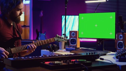 Poster - Male singer learning to play a new song on acoustic guitar, using greenscreen on computer to watch online video tutorials. Artist songwriter practicing with his instrument in home studio. Camera A.