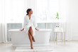 © Prostock-studio - A pretty African American woman enjoys a pampering session in her stylish bathroom. She sits gracefully on the edge of a bathtub, embracing self-care amidst calming decor, copy space
