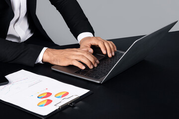 Leinwandbilder - Unrecognizable man in business attire is focused on his laptop, analyzing data. Nearby, a document with colorful pie charts is neatly arranged on the table.