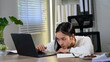 © Parichat - Exhausted asian female entrepreneur suffering from headache and stress while working on a laptop at her home office, overwork and exhaustion concept