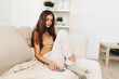 © SHOTPRIME STUDIO - Smiling woman holding mobile phone while relaxing on cozy sofa at home