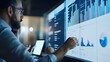 © BerkahStock - Man analyzing data graphs on large screen display.