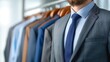 © Vilaysack - A well-dressed man in a suit stands confidently in front of a rack of neatly arranged formal attire.