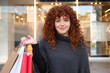 © Cavan Images - Young woman holding shopping bags in front of a store