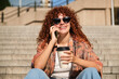 © Cavan Images - Cheerful woman enjoying a phone call and coffee on urban steps