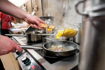 Canvas Print - A chef's hand pours pasta into a pan with clams, creating a flavorful dish in a bustling kitchen. Steam rises, highlighting the vibrant cooking environment and culinary action.