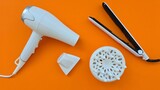 White appliances: hair dryer, nozzles and straightener on an orange background. Devices for creating hairstyles and styling hair