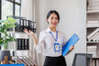 © David - cheerful corporate business Asian woman holding document file and looking at camera stand on a workplace office background.
