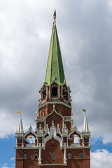 Territory of Moscow castle. Moscow Kremlin tower against background of blue summer sky. Walls are made of red brick. On tower there is huge clock with a black dial. There is ruby ​​star on spire.