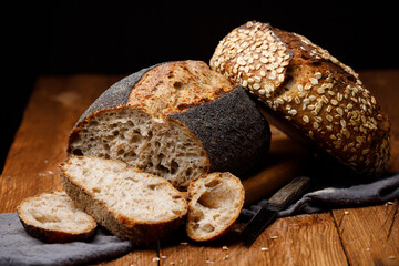 Fototapete - Artisan sliced ​​wheat oat bread and rustic poppy seed bread on wooden table on black background.