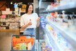 © Serhii - Happy young woman looking at product at grocery store. Smiling woman shopping in supermarket