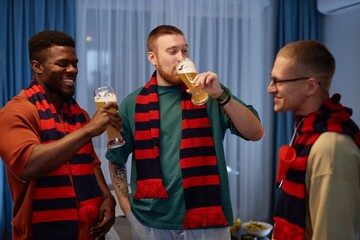 Wall Mural - Waist up portrait of three sports fans laughing and raising beer glasses in toast while celebrating team victory together at home