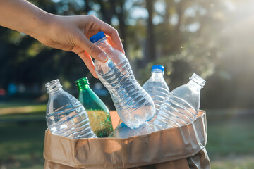 Hand picks plastic bottle from bag amidst sunlit greenery, emphasizing eco friendliness