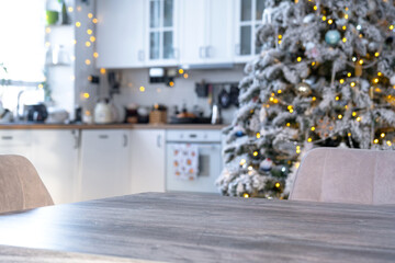 Grey Wooden empty table to demonstrate product with space for text with upholstered chairs in white kitchen, modern interior with Christmas tree and fairy lights. New Year, Christmas mood, cozy home.