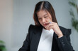 © Tj - Asian businesswoman in black suit thinking and holding pen near her face while working on her project in modern office, business and finance concept