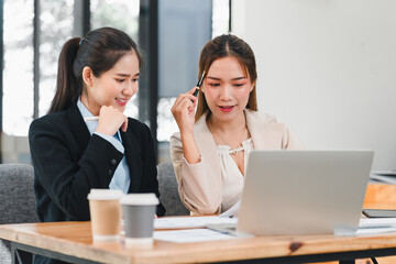 Wall Mural - Two businesswomen discussing work at desk with laptop