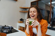 © SHOTPRIME STUDIO - Happy young woman enjoying a green smoothie in a bright kitchen, representing healthy eating and wellness lifestyle, with a warm, inviting atmosphere