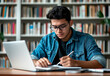 © GustavsMD - Young man wearing glasses and denim jacket studying in a library with a laptop and notebook, surrounded by bookshelves