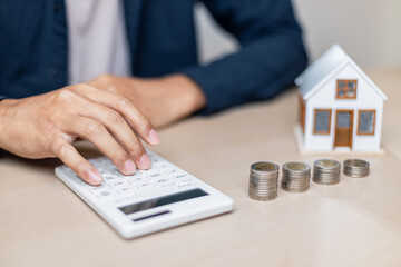 Wall Mural - Person calculating finances with coins and house model on table