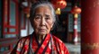 © sevenSkies - Asian elderly woman serious wearing red traditional attire looking on camera
