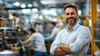 © Rose on Lens - A smiling man stands confidently in a factory setting, with machinery and colleagues working in the background.