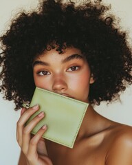 Wall Mural - A portrait of a model with curly hair holding a green wallet, showcasing natural makeup and a soft, inviting expression.