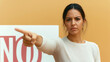 © stock1 - A Latina woman in casual attire points to a bold NO sign with determination, her expression reflecting concern and a desire to raise awareness about a pressing issue