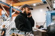 © Maskot - Low angle view of male warehouse worker wearing cap talking on smart phone in manufacturing factory