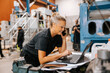 © Maskot - Female warehouse worker talking on smart phone while using laptop in manufacturing factory