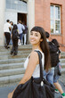 © Maskot - Portrait of smiling woman carrying bag while looking over shoulder at college campus