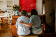 © Maskot - Rear view of female caregiver sitting with arm around senior woman playing piano at home