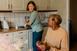 © Maskot - Female nurse washing dishes and while talking with senior man sitting in kitchen at home
