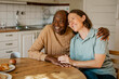 © Maskot - Happy elderly man sitting with arm around female nurse at dining table