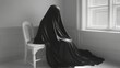 © Aziz - Figure draped in black cloth sits on a chair.