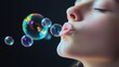 © milenialdesastudio - Close-up of a girl blowing iridescent soap bubbles against a dark background.