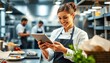 © Maryna - Chef uses tablet in modern kitchen. Staff members prepare food in background. Teamwork, tech in culinary arts. Digital menu order management. Pro environment, focused on food preparation, service.