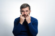 © Niko_Dali - A man with a beard, wearing a blue sweater, uses his fingers to touch the skin around his eyes. He is looking towards the camera against a light gray background.