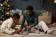 © Seventyfour - Candid scene of happy African American family of father and son playing with toy railroad together on Christmas morning