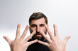 © Niko_Dali - Close-up portrait of a bearded man holding his spread fingers in front of his face against a plain background. His expression is serious.