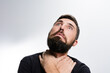 © Niko_Dali - A bearded man against a light background looks upward with wide eyes and a worried expression. His hands are clasped around his neck, suggesting concern or discomfort.