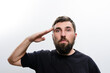 © Niko_Dali - A bearded man in a dark shirt salutes against a plain white backdrop. His expression is serious and focused.