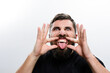 © Niko_Dali - A bearded man stretches his mouth wide with his fingers and sticks out his tongue against a white background.