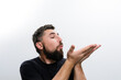 © Niko_Dali - A bearded man in a dark shirt blows a kiss against a white background. He holds his hands cupped together as if sending something delicate into the air.