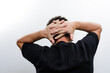 © Niko_Dali - Rear view of a man with his hands clasped behind his head against a plain background. He's wearing a dark t-shirt.