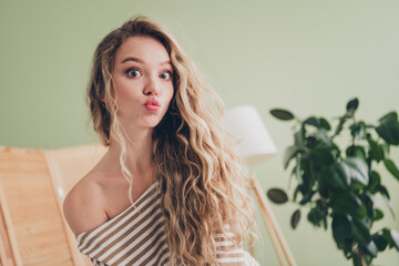 Charming young woman with blond hair making a playful face indoors during a relaxing weekend. She is dressed in a casual striped pullover, reflecting joy and comfort in a cozy living room.