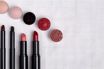 Canvas Print - Lipsticks, lip liners, and blush pans arranged on a white fabric background, flat lay composition for beauty and makeup design

