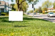 © Maryna - Blank yard sign stands in grassy area near city street on sunny day. Blank white sign ready for message advertisement. Green grass surrounds sign. Residential houses, cars visible on blurred